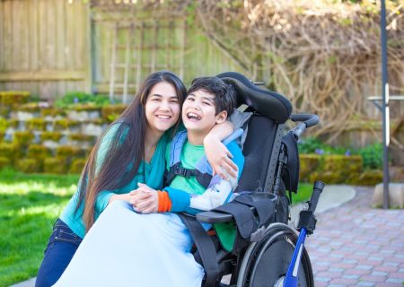 Teenage girl hugging disabled brother in wheelchair outdoors